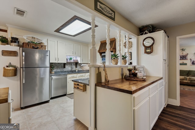 kitchen with wooden counters, appliances with stainless steel finishes, decorative backsplash, sink, and white cabinetry