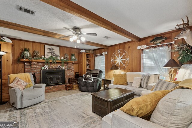 living room with ceiling fan, beamed ceiling, a textured ceiling, wooden walls, and light tile patterned flooring