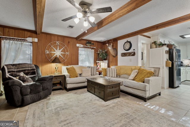 tiled living room with beam ceiling, ceiling fan, wood walls, a textured ceiling, and ornamental molding