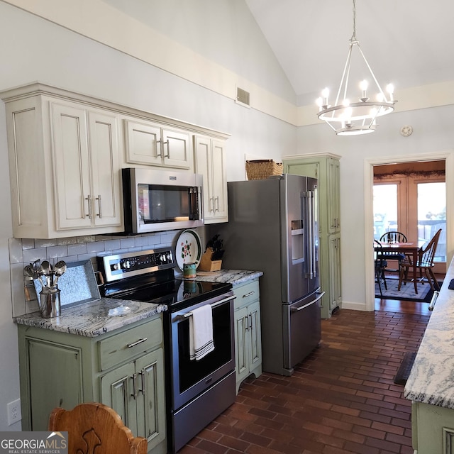 kitchen featuring lofted ceiling, light stone countertops, pendant lighting, appliances with stainless steel finishes, and tasteful backsplash