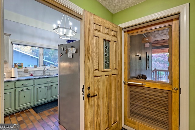 kitchen with hanging light fixtures, sink, stainless steel fridge, a chandelier, and a textured ceiling