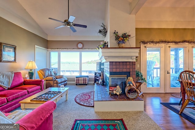 living room with ceiling fan, hardwood / wood-style flooring, high vaulted ceiling, a tile fireplace, and french doors