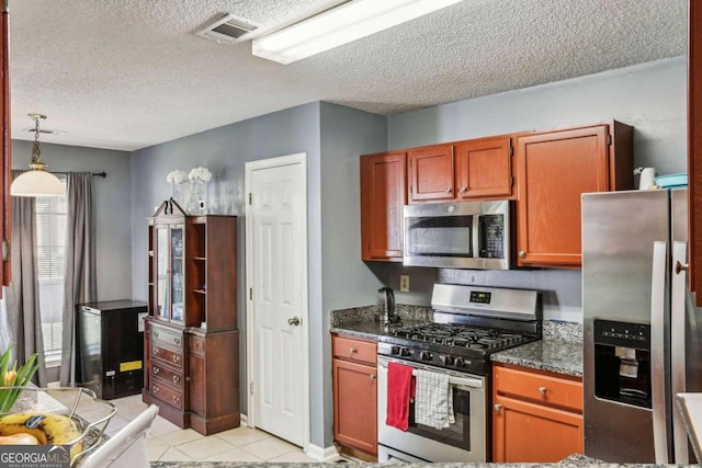 kitchen featuring light tile patterned floors, stainless steel appliances, a textured ceiling, and decorative light fixtures