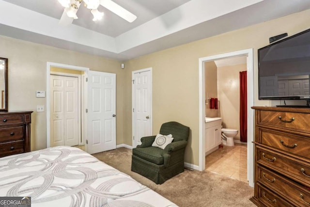 bedroom with a tray ceiling, light colored carpet, connected bathroom, and ceiling fan