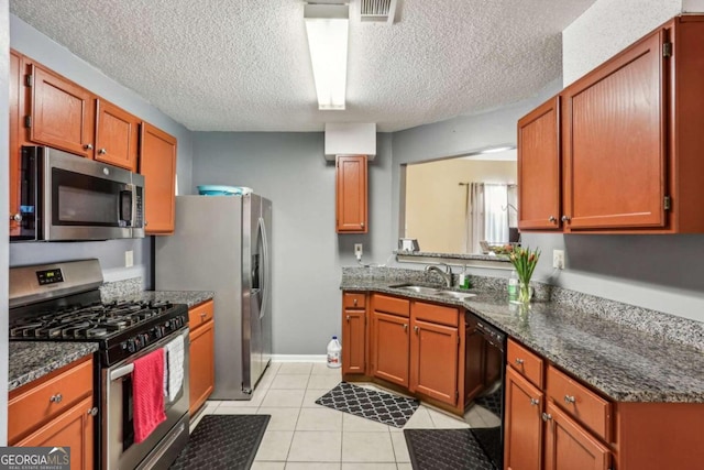 kitchen with stainless steel appliances, dark stone counters, sink, light tile patterned floors, and a textured ceiling