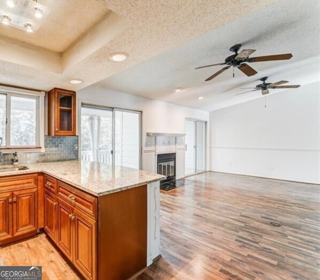 kitchen with a textured ceiling, light stone countertops, light wood-type flooring, and a raised ceiling