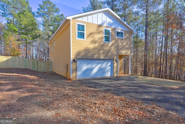 view of side of property featuring aphalt driveway, board and batten siding, a garage, and fence