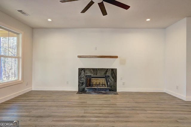 unfurnished living room with recessed lighting, a premium fireplace, wood finished floors, visible vents, and baseboards