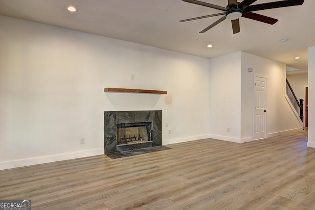 unfurnished living room featuring light wood-style floors, baseboards, stairway, and a high end fireplace