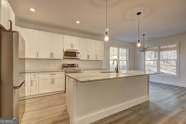 kitchen featuring decorative light fixtures, appliances with stainless steel finishes, white cabinets, a sink, and an island with sink