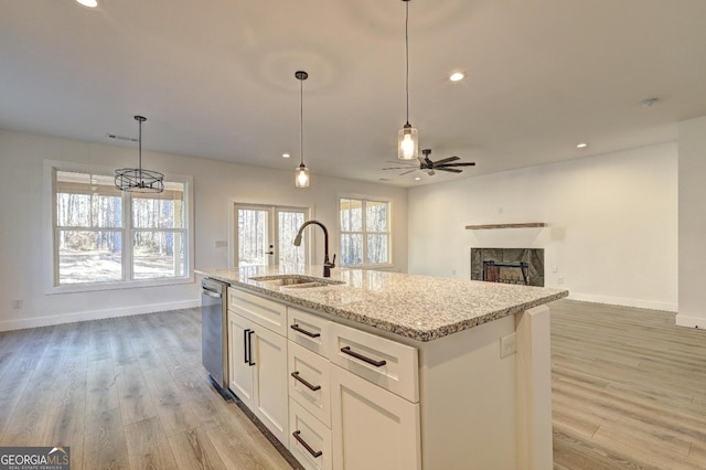 kitchen featuring a center island with sink, open floor plan, stainless steel dishwasher, pendant lighting, and a sink