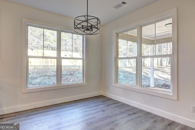 unfurnished dining area featuring baseboards, plenty of natural light, visible vents, and wood finished floors