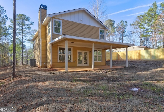 back of house featuring board and batten siding, cooling unit, fence, and a chimney