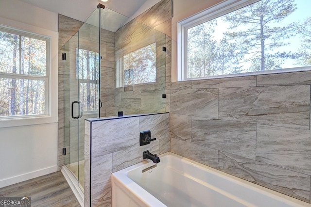 bathroom with a bath, a shower stall, baseboards, and wood finished floors