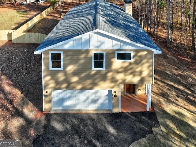 view of property exterior with board and batten siding, driveway, a shingled roof, and a chimney