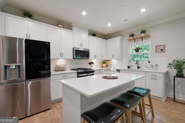 kitchen with white cabinetry, stainless steel appliances, a kitchen breakfast bar, light hardwood / wood-style floors, and a kitchen island