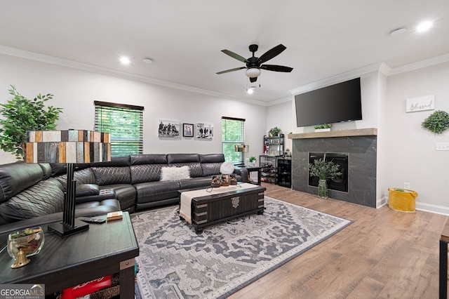 living room featuring a tiled fireplace, crown molding, ceiling fan, and light wood-type flooring