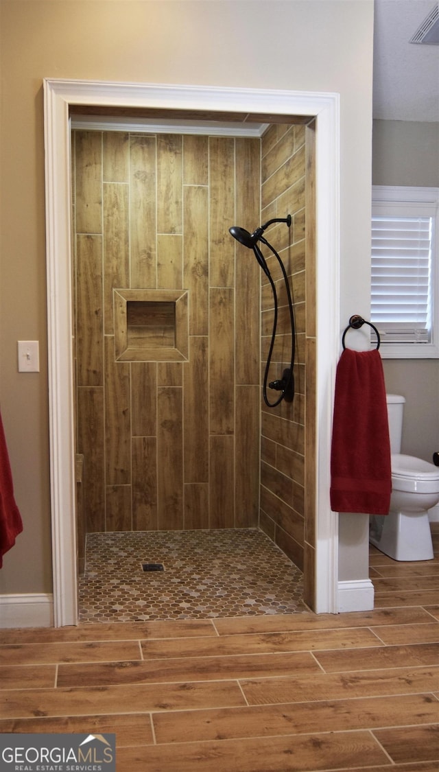 bathroom featuring tiled shower, wood-type flooring, and toilet