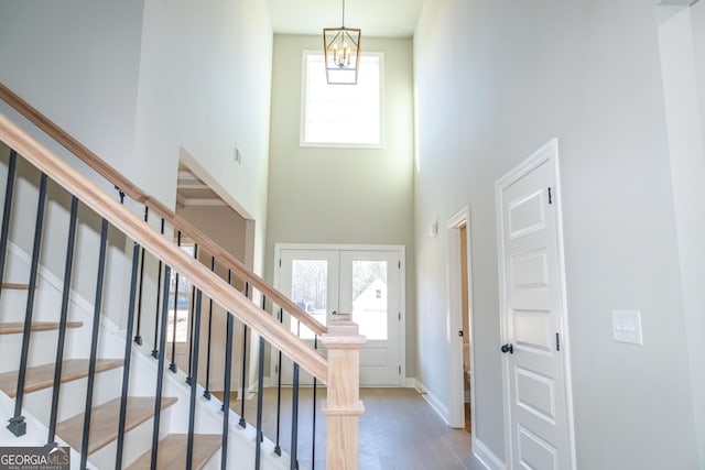 entryway featuring french doors, a towering ceiling, hardwood / wood-style flooring, and a notable chandelier