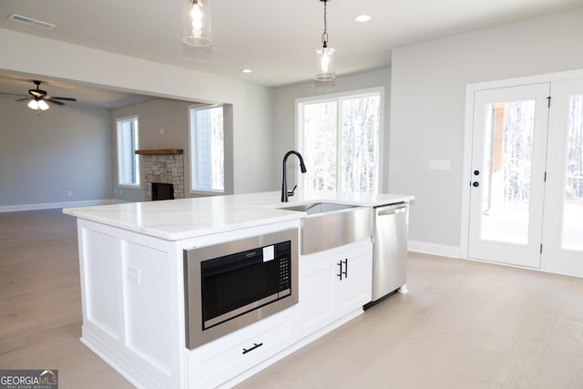 kitchen featuring stainless steel dishwasher, built in microwave, sink, pendant lighting, and an island with sink