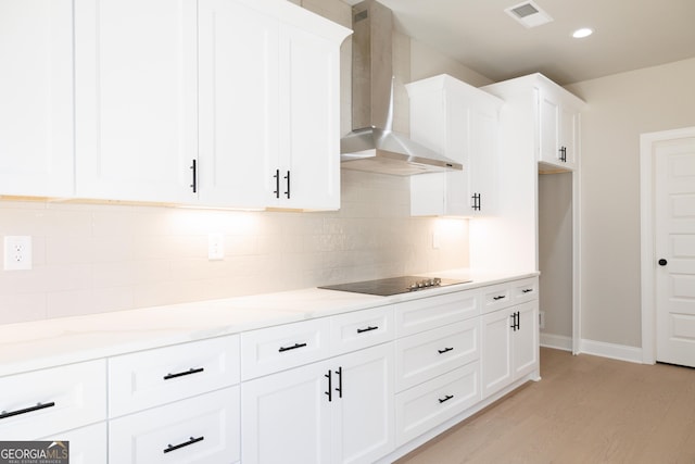 kitchen featuring white cabinets, wall chimney range hood, light wood-type flooring, black electric cooktop, and light stone counters