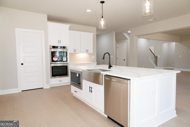 kitchen featuring a center island with sink, pendant lighting, white cabinets, and appliances with stainless steel finishes