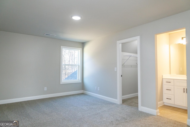 unfurnished bedroom featuring a walk in closet, connected bathroom, light colored carpet, and a closet