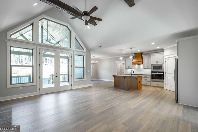 kitchen featuring white cabinetry, stainless steel appliances, decorative light fixtures, a center island with sink, and custom range hood