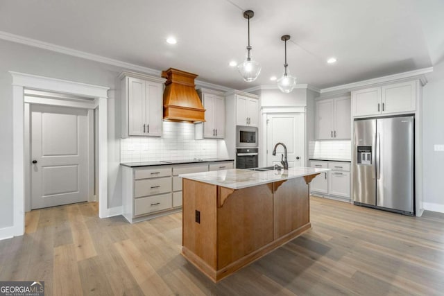 kitchen with light wood-type flooring, custom exhaust hood, stainless steel appliances, a center island with sink, and a breakfast bar area