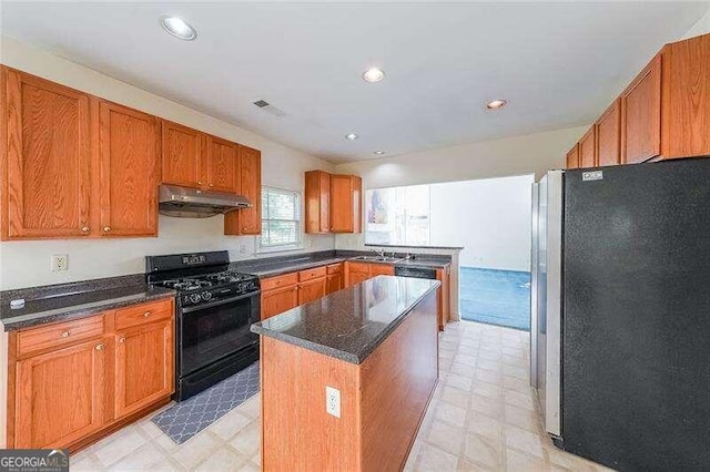 kitchen featuring sink, a center island, black gas range oven, dark stone counters, and stainless steel refrigerator