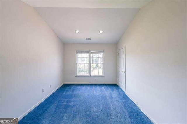 spare room featuring vaulted ceiling and dark colored carpet