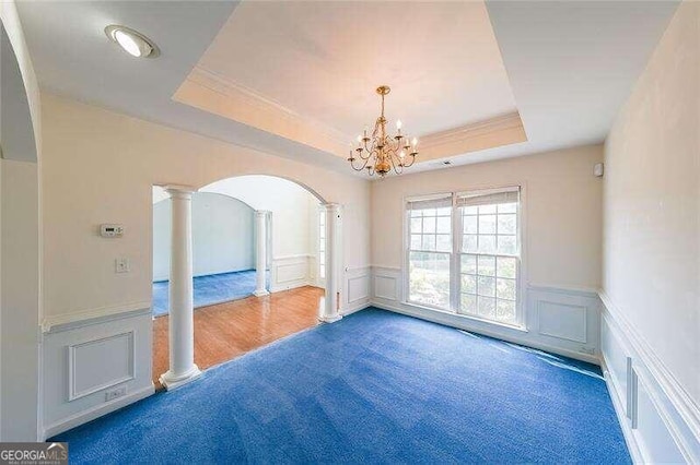 carpeted empty room with decorative columns, a chandelier, and a raised ceiling