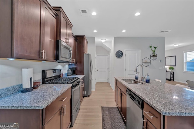 kitchen with appliances with stainless steel finishes, light stone countertops, a kitchen island with sink, light hardwood / wood-style flooring, and sink