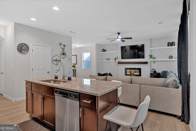 kitchen with an island with sink, light hardwood / wood-style flooring, sink, light stone countertops, and stainless steel dishwasher