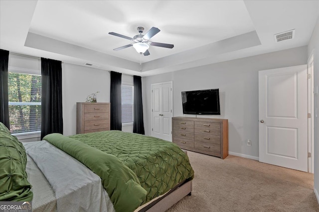 bedroom featuring light carpet, a tray ceiling, and ceiling fan