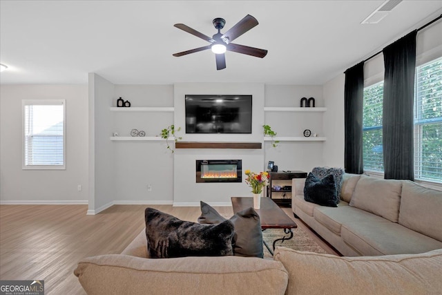 living room featuring built in features, light hardwood / wood-style floors, a healthy amount of sunlight, and ceiling fan