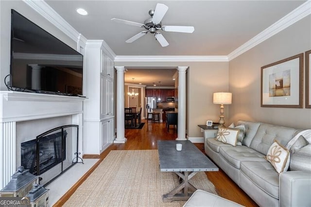 living room featuring ornate columns, ornamental molding, hardwood / wood-style flooring, and ceiling fan with notable chandelier