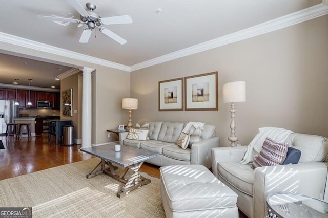 living room featuring dark wood-type flooring, ceiling fan, crown molding, and ornate columns