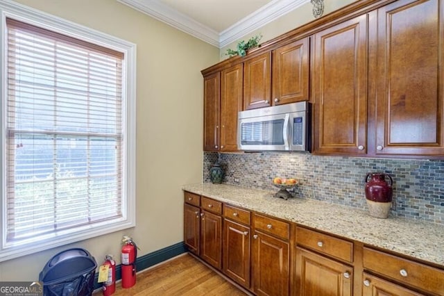 kitchen with crown molding, light stone countertops, light hardwood / wood-style flooring, and backsplash