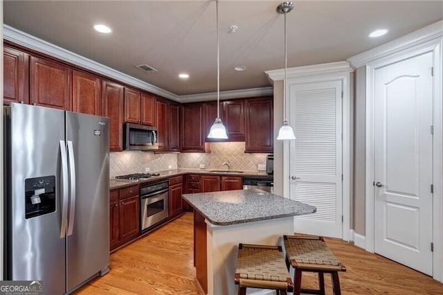 kitchen featuring appliances with stainless steel finishes, light hardwood / wood-style flooring, a kitchen island, and pendant lighting