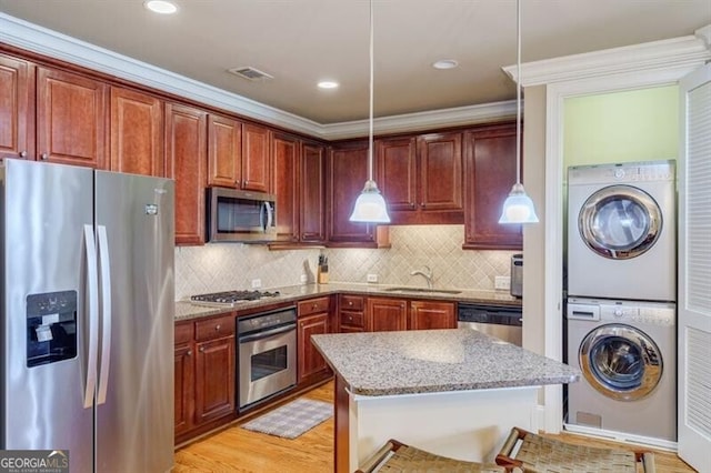 kitchen featuring light stone countertops, stainless steel appliances, sink, decorative light fixtures, and stacked washer and clothes dryer