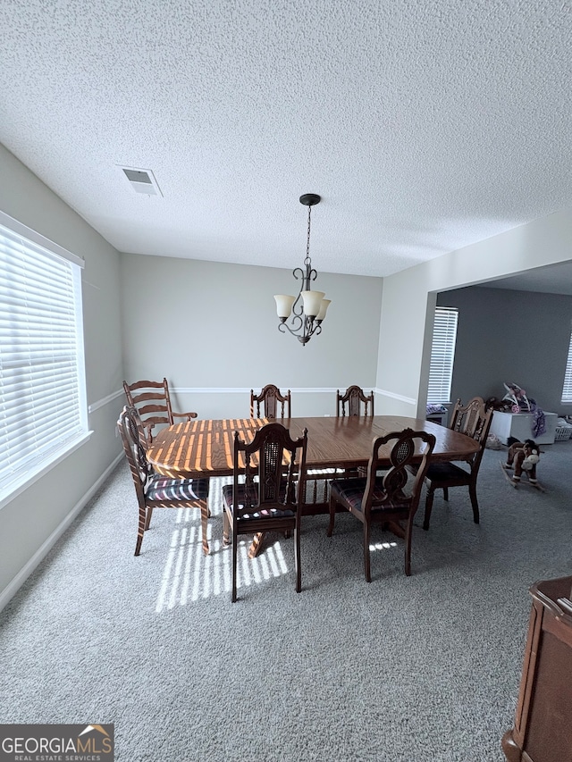 dining area with a textured ceiling, carpet floors, and an inviting chandelier