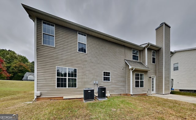 back of house with central air condition unit and a lawn