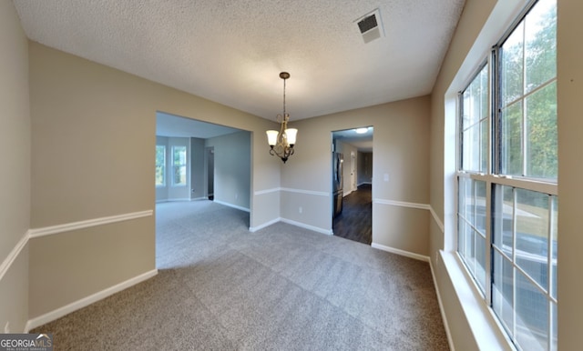 carpeted spare room with a notable chandelier and a textured ceiling