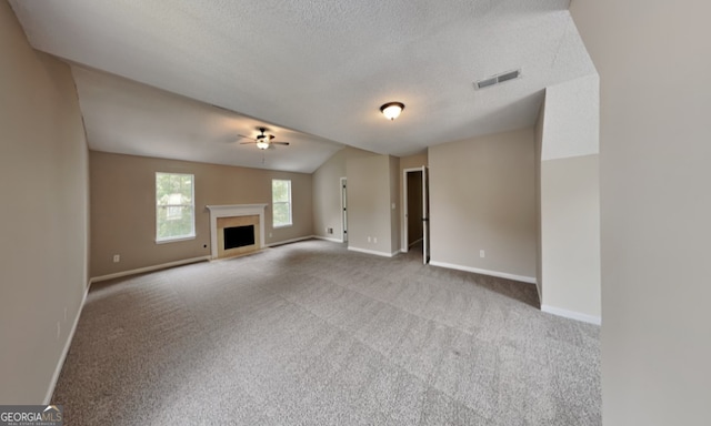 unfurnished living room with lofted ceiling, a textured ceiling, light colored carpet, and ceiling fan