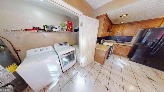 laundry area with a textured ceiling, light tile patterned flooring, water heater, and washing machine and dryer