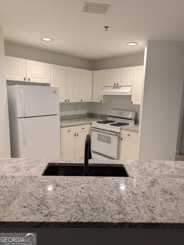 kitchen with white cabinetry, light stone countertops, and white appliances