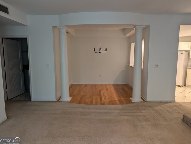 unfurnished dining area featuring ornate columns, light wood-type flooring, and a chandelier