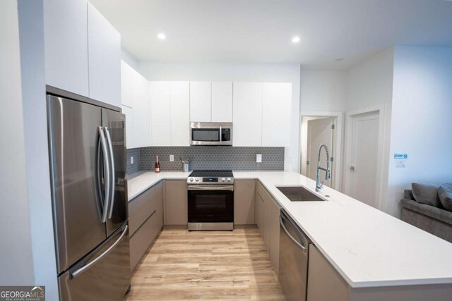 kitchen with white cabinets, backsplash, appliances with stainless steel finishes, light hardwood / wood-style flooring, and sink