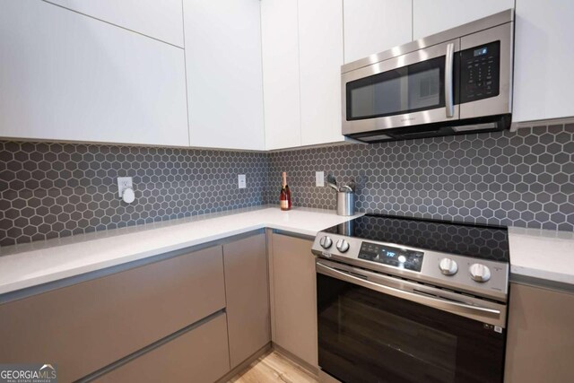 kitchen with light hardwood / wood-style floors, stainless steel appliances, tasteful backsplash, and white cabinets